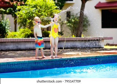 Kids Playing With Garden Hose In Backyard With Large Outdoor Swimming Pool. Children Play With Water. Swim Wear And Toys For Boy And Girl. Family Summer Vacation With Hot Sunny Weather. Garden Pool.