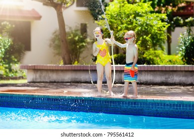 Kids Playing With Garden Hose In Backyard With Large Outdoor Swimming Pool. Children Play With Water. Swim Wear And Toys For Boy And Girl. Family Summer Vacation With Hot Sunny Weather. Garden Pool.