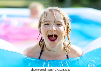 Kids Playing In Inflatable Pool In The Garden. Children Swim And Splash In Blue Swimming-pool. Happy Little Girl Playing With Water On Hot Sunny Summer Day. Family Having Fun Outdoors In The Backyard.