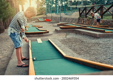 Kids Playing Mini Golf On Summer Evening On The Territory Of The Hotel