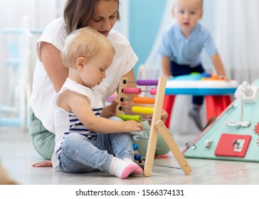 Kids playing on floor with developmental toys in kindergarten. Children have fun in nursery or daycare. Babies with teacher in creche
