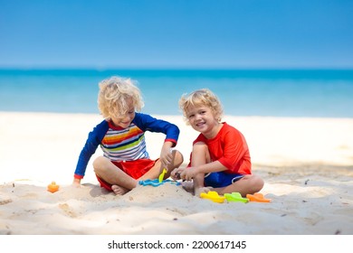 Kids playing on tropical beach. Children play at sea on summer family vacation. Sand and water toys, sun protection for young child. Little boy digging sand, building castle at ocean shore. - Powered by Shutterstock