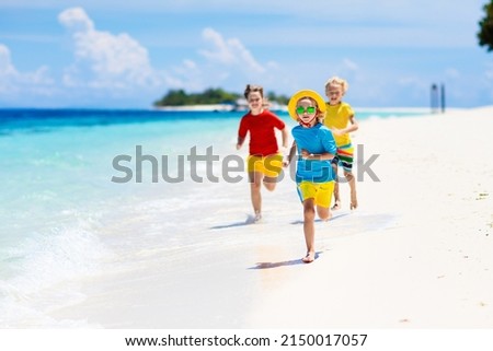 Kids playing on tropical beach. Children swim and play at sea on summer family vacation. Sand and water fun, sun protection. Little child running and jumping at ocean shore.