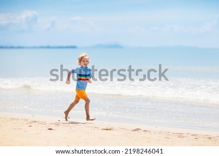 Kids playing on tropical beach. Children swim and play at sea on summer family vacation. Sand and water fun, sun protection for young child. Little boy running and jumping at ocean shore.