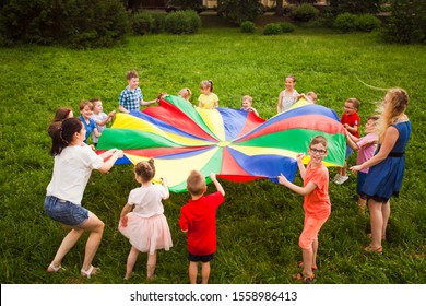 Kids Playing With Rainbow Parachute In The Park