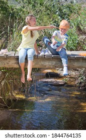 Kids Playing While Sitting On A Wooden Bridge Over A Stream With A Fishing Net