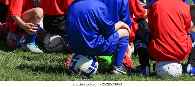 Kids preparing for their soccer training listning to the coach while sitting on their soccer balls - Powered by Shutterstock