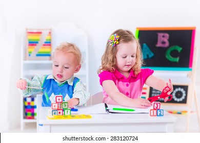 Kids At Preschool. Two Children Drawing And Painting At Kindergarten. Boy And Girl Happy To Go Back To School. Toddler Kid And Baby Learn Letters At Child Care. Class Room With Chalkboard And Abacus