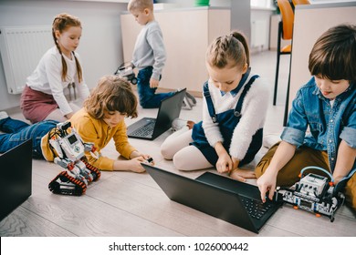 kids programming diy robots with laptops while sitting on floor, stem education concept