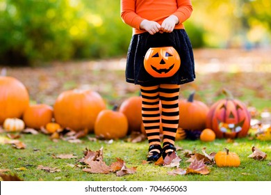 Kids With Pumpkin On Halloween. Little Girl In Witch Costume And Hat Playing In Autumn Park. Child At Halloween Trick Or Treat. Kid Trick Or Treating. Toddler With Lantern. Children With Candy Bucket.