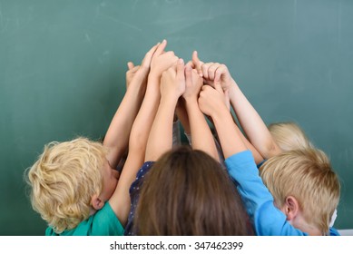 Kids Raising Their Arms At The Center Together And Showing Thumbs Up Hand Signs Against Green Chalkboard.