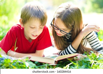 Kids Reading Together Enjoying A Book Laying On The Grass Outdoors