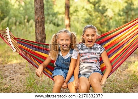 Kids relax in colorful rainbow hammock. Hot day garden outdoor fun. Afternoon nap during summer vacation. Children relaxing.