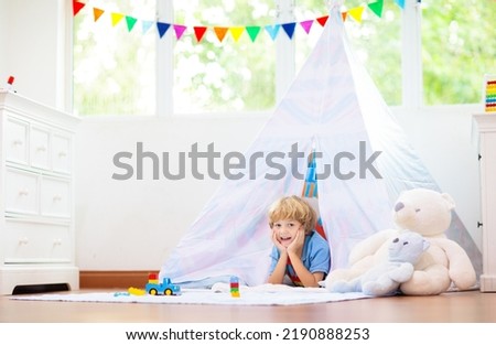 Kids room with teepee tent. Children play in white sunny bedroom. Cozy light interior for kid nursery or playroom. Little boy with toy blocks and dinosaur playing on wooden floor. Home decoration.