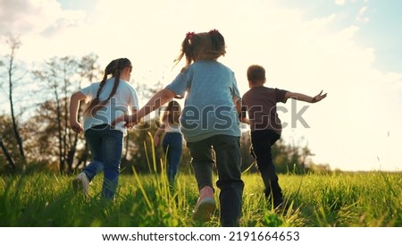 kids run in the park. a large group of a team of children running back view sunlight in the summer on the grass in the park camera movement. people in the park happy family kid lifestyle dream