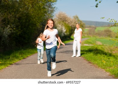 kids running down a path in spring, their pregnant mother standing in the background