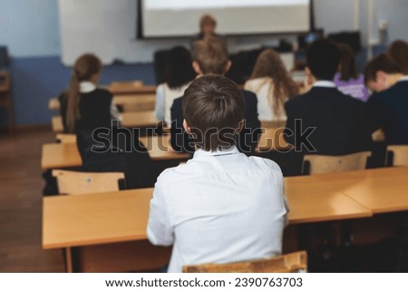 Kids in school writing and taking notes, teens pupils behind desks during the lesson listen to teacher lecture, classroom with students and classmates, group of teenagers during test and exam