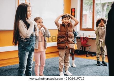 Kids sing and move along to an educational rhyme in class. Group of primary school children participating in a class activity with the instruction of the teacher. Students learning in a co-ed school. Foto stock © 