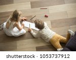 Kids sister and brother playing drawing together on wooden warm floor in living room, creative children boy and girl having fun at home, siblings friendship, underfloor heating concept, top view