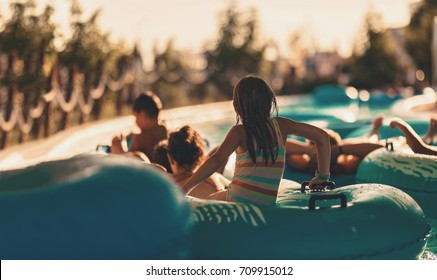 Kids sit in the sun, float in a glimpse into the glorious sunlight from the sunset on the artificial river created in the aquatic fun park, kids are happy with friends any familiy