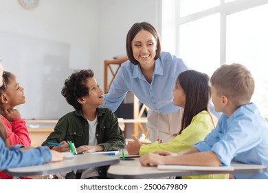 Kids sitting at desks in classroom and listening their teacher, woman explaining something interesting to pupils, studying at school - Powered by Shutterstock