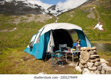 Kids, Sitting In Front Of A Piched Tent In Nature, Eating, Enjoying Wild Camping. Family Vacation