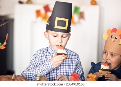 Kids Sitting On Festive Table And Celebrating Thanksgiving Day. Children In Paper Turkey Hat And Pilgrim Hats Eating Cupcakes And Drinking Milk.