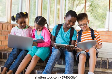 Kids sitting on staircase using laptop and digital tablet at school - Powered by Shutterstock