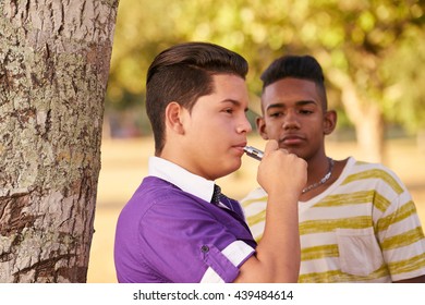 Kids Smoking Electronic Cigarette In Park. Concept Of Health Problems And Social Issues Between Young People