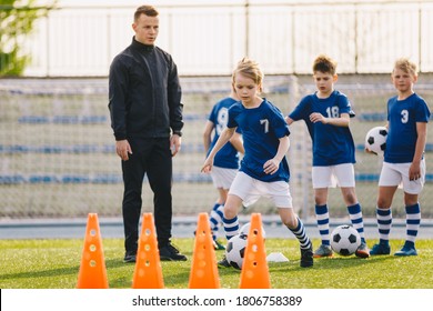 Kids In Soccer Team On Practice Session With Young Coach. Boys Young Athletes Training Football On Grass Field. Kids Kicking Balls And Running Fast During Soccer Training Camp