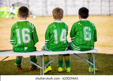 Kids Soccer Team. Youth Soccer Coaching Picture. Soccer Practice Match And Game Day. Young Boys Substitute Players Sitting On Bench And Watching Youth Soccer Training Match