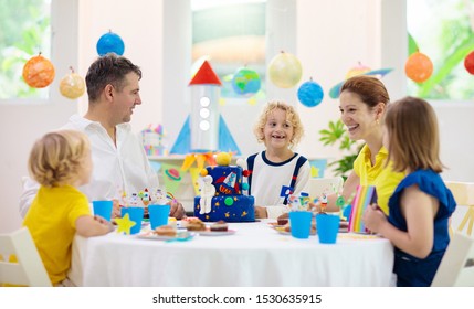 Kids space theme birthday party with cake and cupcakes. Rocket, solar system planet and astronaut decoration for child event. Little boy, friends and parents blowing candles and opening presents. - Shutterstock ID 1530635915