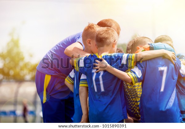 Kids sport team having pep talk\
with coach. Children soccer team motivated by trainer. Coaching\
football youth team. Young boys standing together\
united