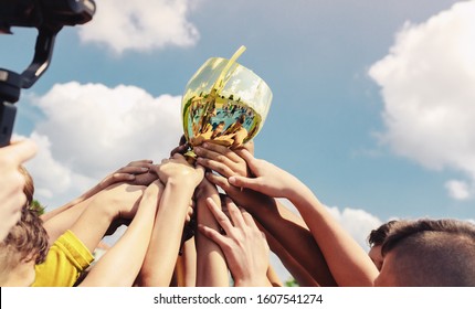 Kids in sports team lift up the golden cup trophy after winning the final tournament match. Children celebrate success in sports. Winning championship in sports