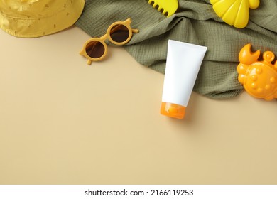 Kids sunscreen cream tube with sunglasses, panama hat, towel, sand molds on beige background.