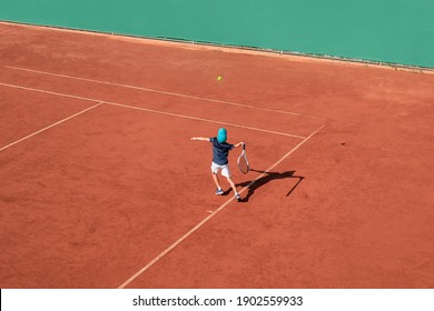 Kids tennis sport concept. Child tennis player performs service on red clay court. Boy athlete in action. High view from above, background, copy space