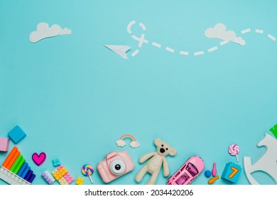 Kids toy background. Variety of plastic and wooden kids toys on blue background with paper plane and clouds. Top view, flat lay.