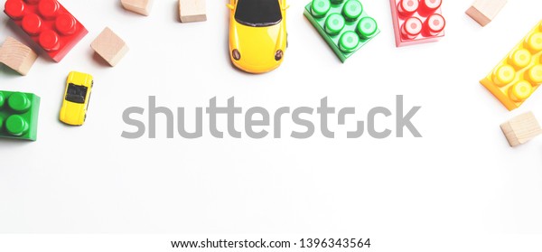 Kids toys frame with toy cars, plastic bricks\
and wooden blocks on white\
background