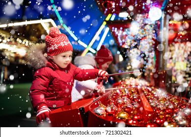 Kids at traditional Christmas fair. Children and Xmas market on snowy evening. Family shopping Christmas gifts and presents. Boy and girl play hook a bauble game. Winter fun. Advent time in Europe. - Powered by Shutterstock