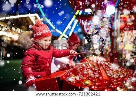 Kids at traditional Christmas fair. Children and Xmas market on snowy evening. Family shopping Christmas gifts and presents. Boy and girl play hook a bauble game. Winter fun. Advent time in Europe.