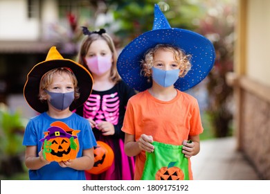 Kids Trick Or Treat In Halloween Costume And Face Mask. Children In Dress Up With Candy Bucket In Coronavirus Pandemic. Little Boy And Girl Trick Or Treating With Pumpkin Lantern. Autumn Holiday Fun.