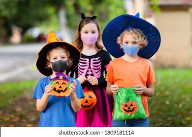 Kids Trick Or Treat In Halloween Costume And Face Mask. Children In Dress Up With Candy Bucket In Coronavirus Pandemic. Little Boy And Girl Trick Or Treating With Pumpkin Lantern. Autumn Holiday Fun.