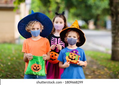 Kids Trick Or Treat In Halloween Costume And Face Mask. Children In Dress Up With Candy Bucket In Coronavirus Pandemic. Little Boy And Girl Trick Or Treating With Pumpkin Lantern. Autumn Holiday Fun.