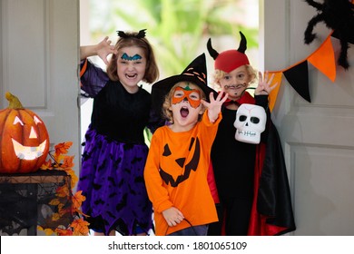 Kids trick or treat on Halloween night. Child at decorated house door. Boy and girl in witch and vampire costume and hat with candy bucket and pumpkin lantern. Autumn decoration. Friends play. - Powered by Shutterstock