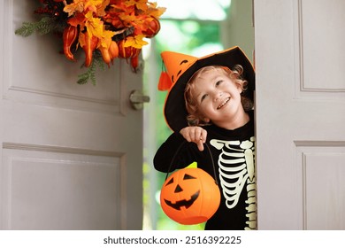 Kids trick or treat on Halloween night. Child at decorated house door with autumn leaf wreath and pumpkin lantern. Little boy in witch and skeleton costume and hat with candy bucket. Fall decoration.  - Powered by Shutterstock