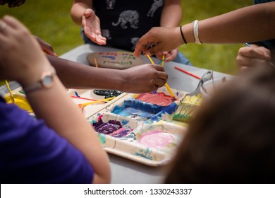 Kids Use Different Colors Of Paint To Create Art Projects Outside. They Have Different Brushes And Things To Paint On Rocks Outside. 