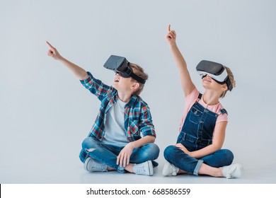 kids using virtual reality headsets and pointing up with finger while sitting on the floor - Powered by Shutterstock