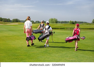 Kids walking on fairway with bags at golf school, back view