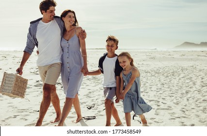 Kids Walking With Their Parent Along The Beach On Summer Day. Family Of Four At Beach For A Picnic.