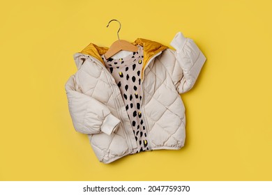 Kids Warm Puffer Jacket Hanging On A Hanger On Yellow  Background. Stylish Childrens Outerwear. Winter Fashion Outfit 